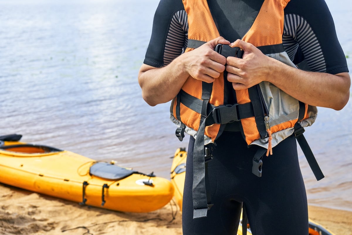 Male hiker wearing wetsuit putting on a life vest