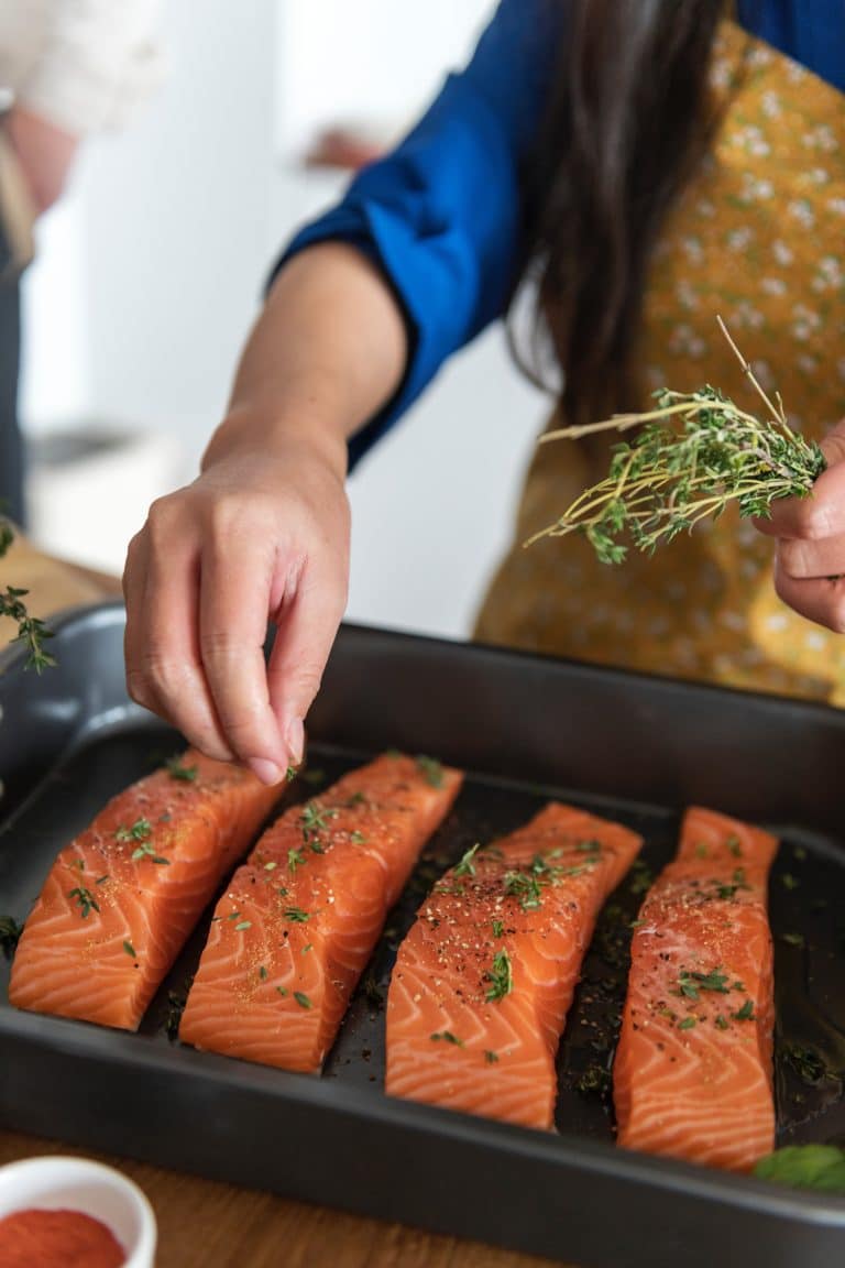 person seasoning salmon in a non-stick tray before cooking