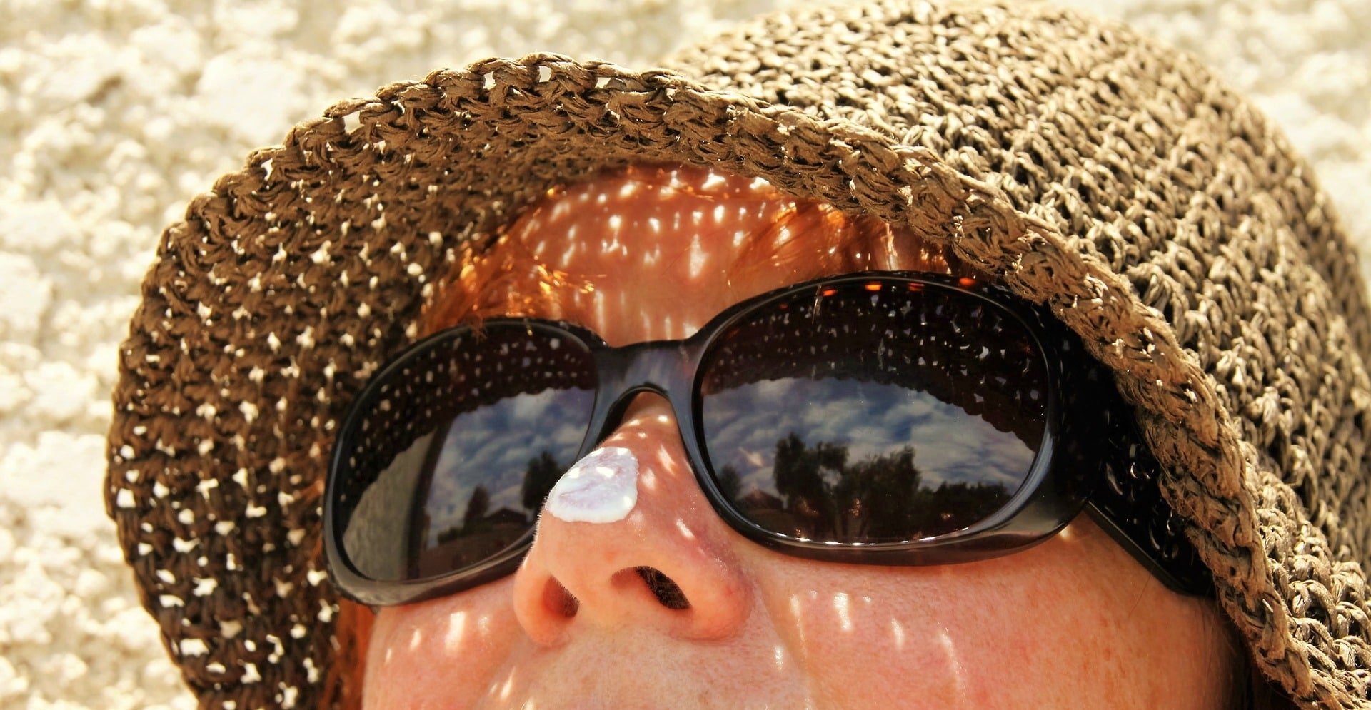 Woman in hat wearing sunglasses with sunscreen on nose