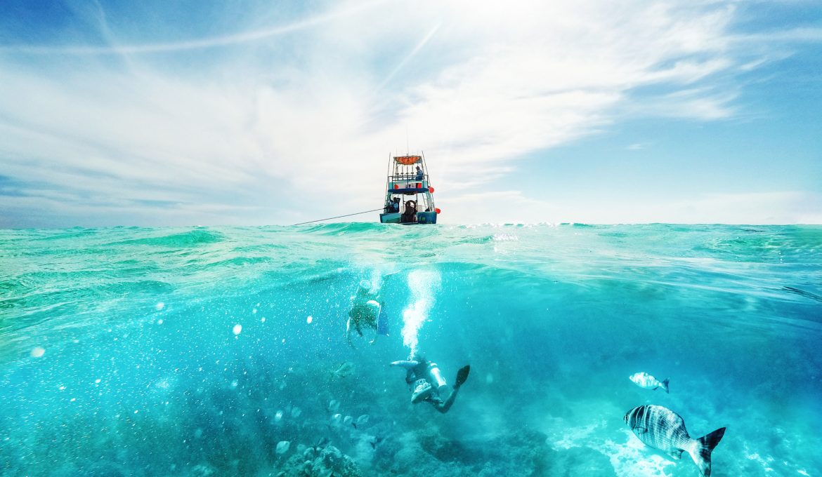Scuba divers underwater and fishing tour boat above the Caribbean Sea in Cozumel, Mexico