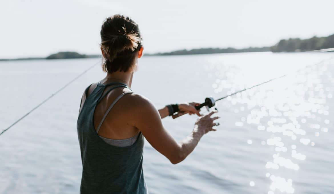 Woman in gray tank top with fishing rod standing on shore