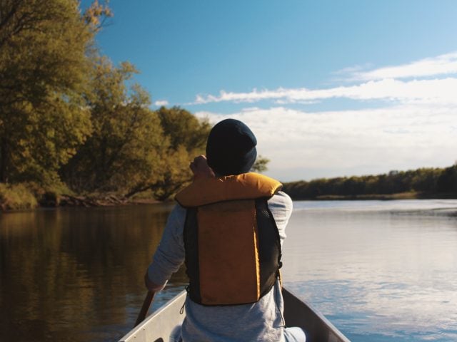 Man in yellow life jacket and black hat canoeing during fall